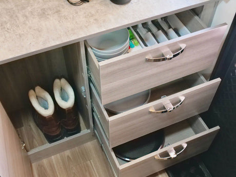 Inside an RV rental: compact kitchen storage with organized drawers for cutlery, dishes, and a boot cubby.