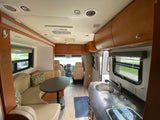Bright RV rental interior featuring a kitchen, dining booth, and cockpit. Ideal for comfortable mobile living on road trips.