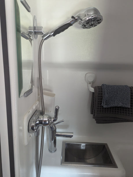 RV rental's compact bathroom includes a shower, sink, mirror, and towels. Functional design for mobile living.
