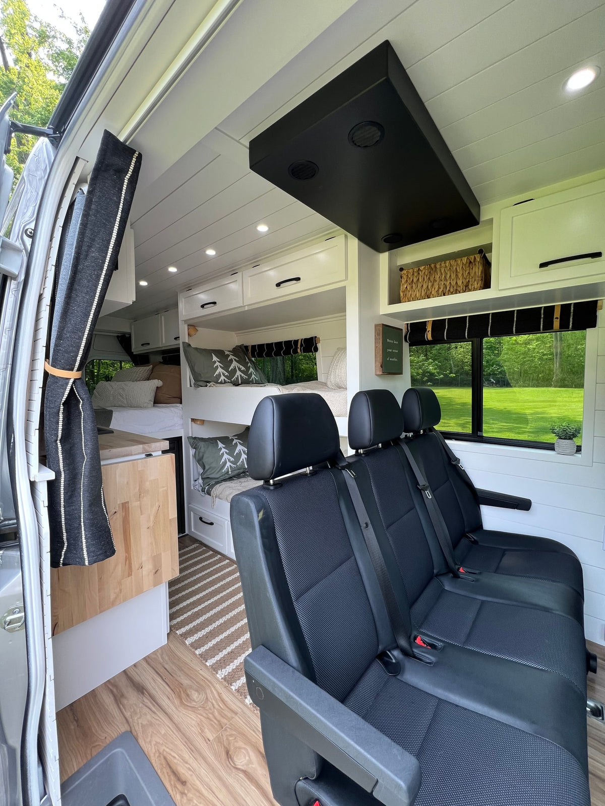 RV rental: Bright campervan interior with bunk beds, passenger seating, white shiplap walls, and wood-look flooring.