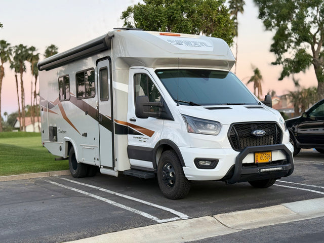 White Coachmen Cross Trail RV rental, a Ford Transit-based motorhome with a front brush guard, is parked. Ready for travel adventures.