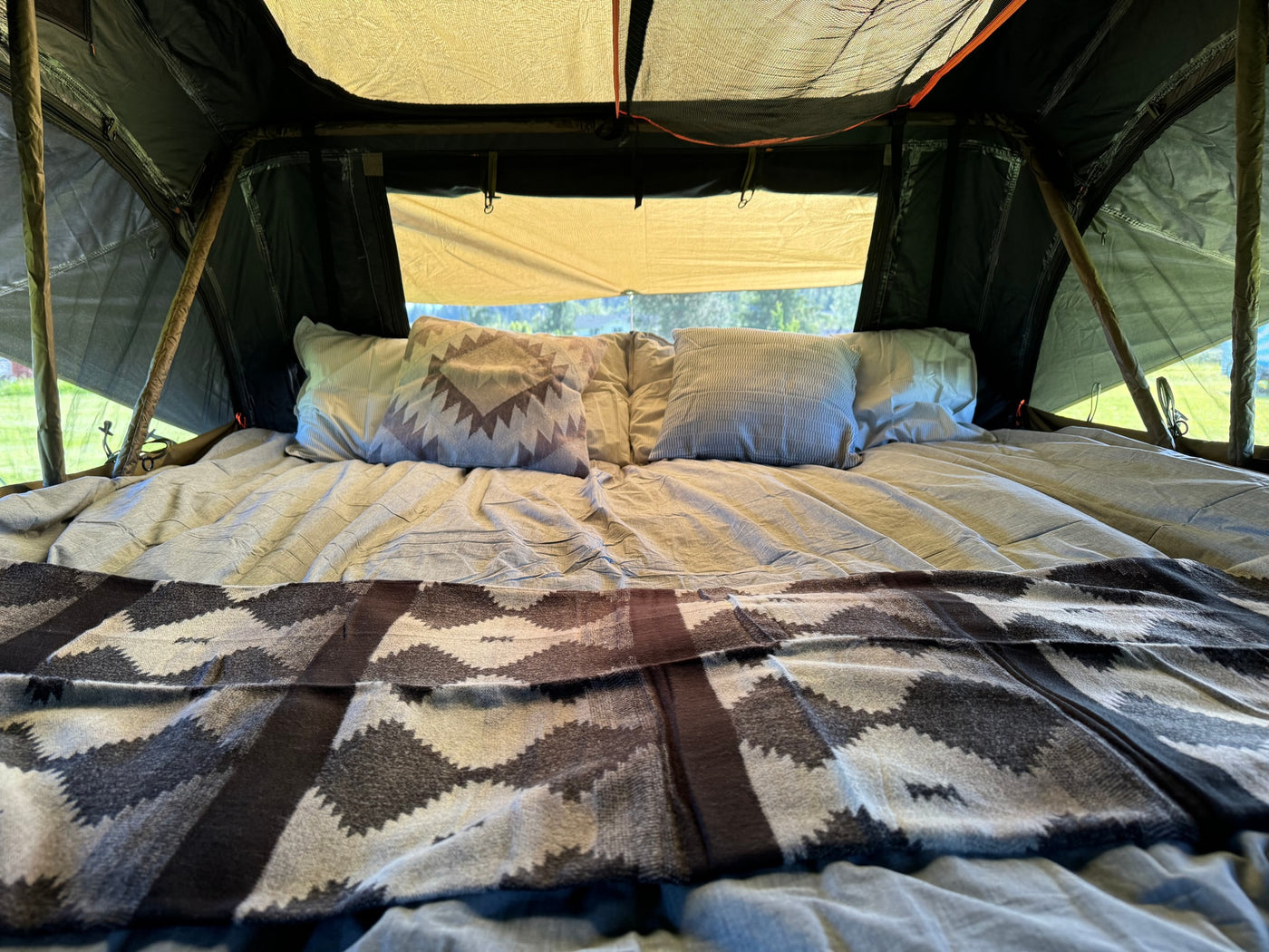 Cozy bed set up inside a tent with pillows and patterned blanket, ready for an RV rental adventure. — photo 12
