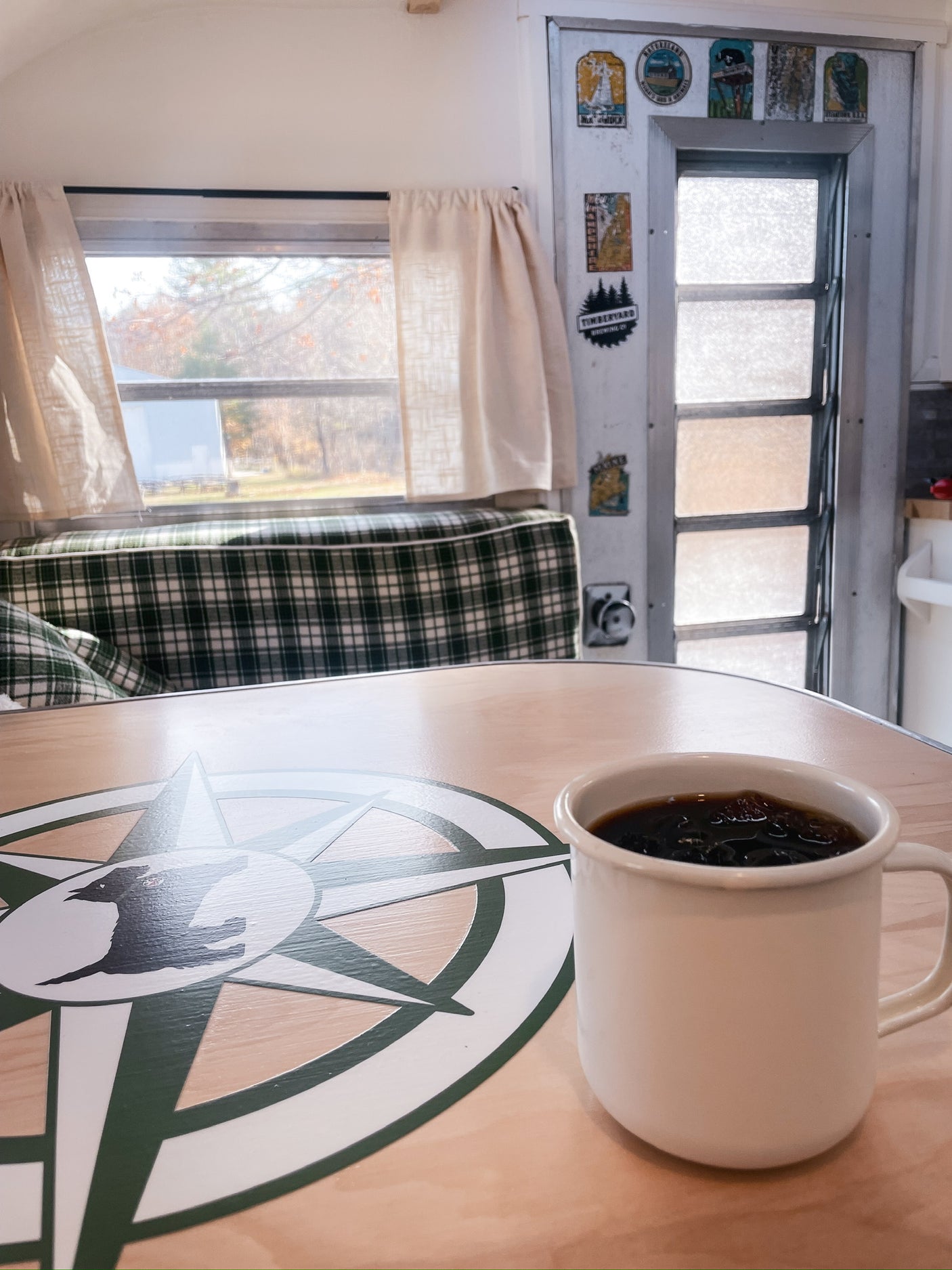 Coffee in an RV rental, showing a cozy interior with plaid seating, a compass table, and a window view of autumn trees.
