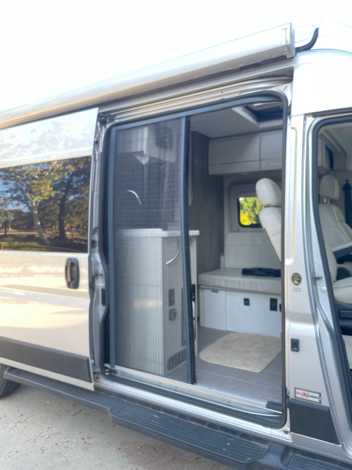 This RV rental camper van with its open side door showcases the compact interior, including a screen and versatile seating.