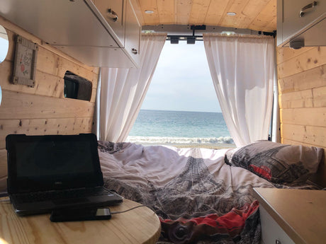Cozy RV rental interior with a bed, laptop, and an incredible beach view. Perfect for remote work or relaxation by the ocean.