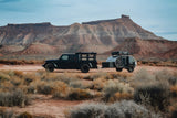 Dark Jeep Gladiator towing a sleek teardrop RV rental. Perfect for desert adventures amidst red rock mountains.