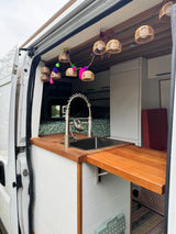 Step inside this rv rental camper van kitchen! It boasts a sink, wood counters, and charming string lights for travel.