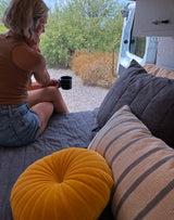 Cozy RV rental setup. Woman sips coffee, gazing at a serene outdoor view from the comfort of her travel home.