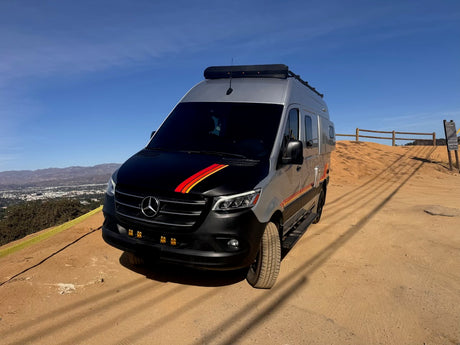Stunning Mercedes Sprinter adventure van, ideal for your next RV rental journey. Parked on a scenic dirt hill overlooking a city.