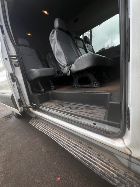Spacious RV rental interior featuring gray passenger seats, wood-look floor, and wide entry step visible through the open sliding door.