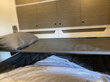 RV rental interior features bunk beds, with a pillow on the top cot-style bed and overhead storage cabinets.