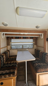 RV rental interior: A cozy dinette features patterned bench seating, a central table, window blinds, and ceiling lights.