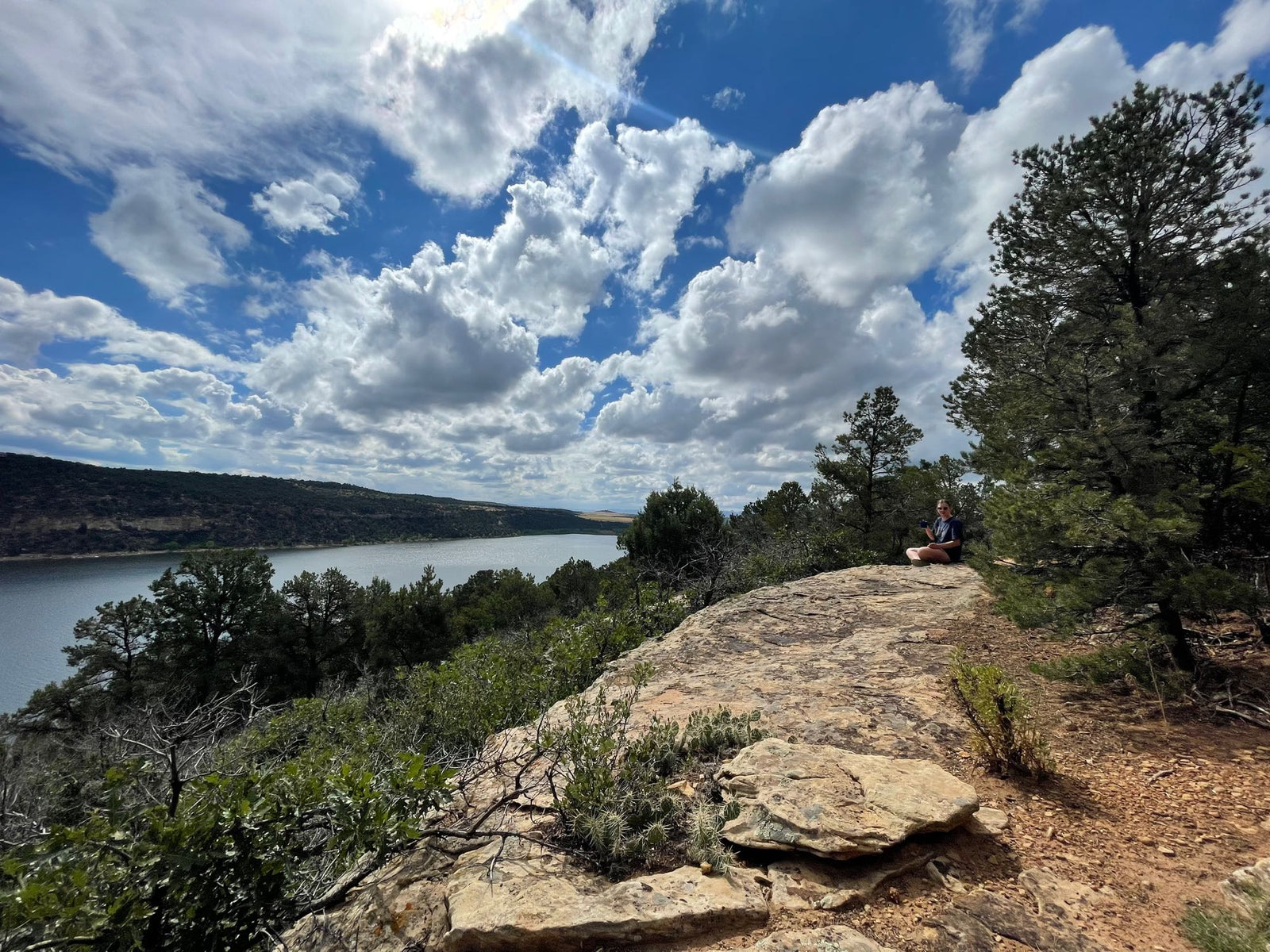 Stunning cliffside lake view with a person meditating. Imagine this peaceful spot on your next RV rental adventure.