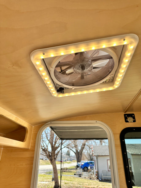RV rental with a bright, wood-paneled interior, featuring an LED-lit ceiling fan and an outside view through the window.