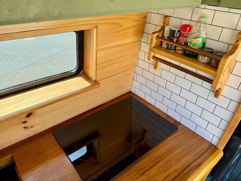 Compact RV rental kitchen features wooden walls, a sleek induction cooktop, subway tile backsplash, and a handy spice rack. — photo 13