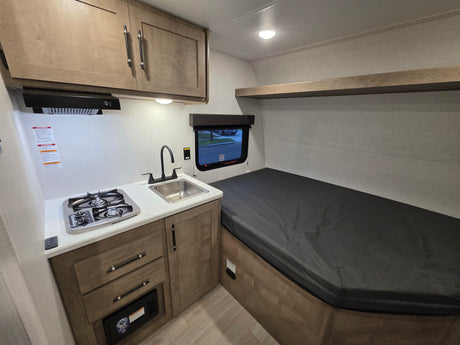 This RV rental offers a compact interior with a kitchen area featuring a stove, sink, and cabinets, plus a comfortable bed.
