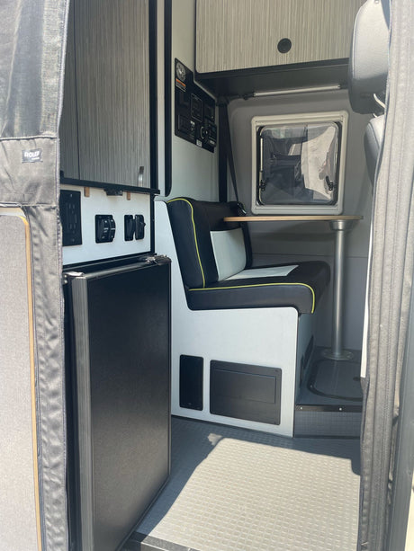 Functional RV rental interior featuring a compact kitchenette with fridge and a dinette with bench seating and a small table.