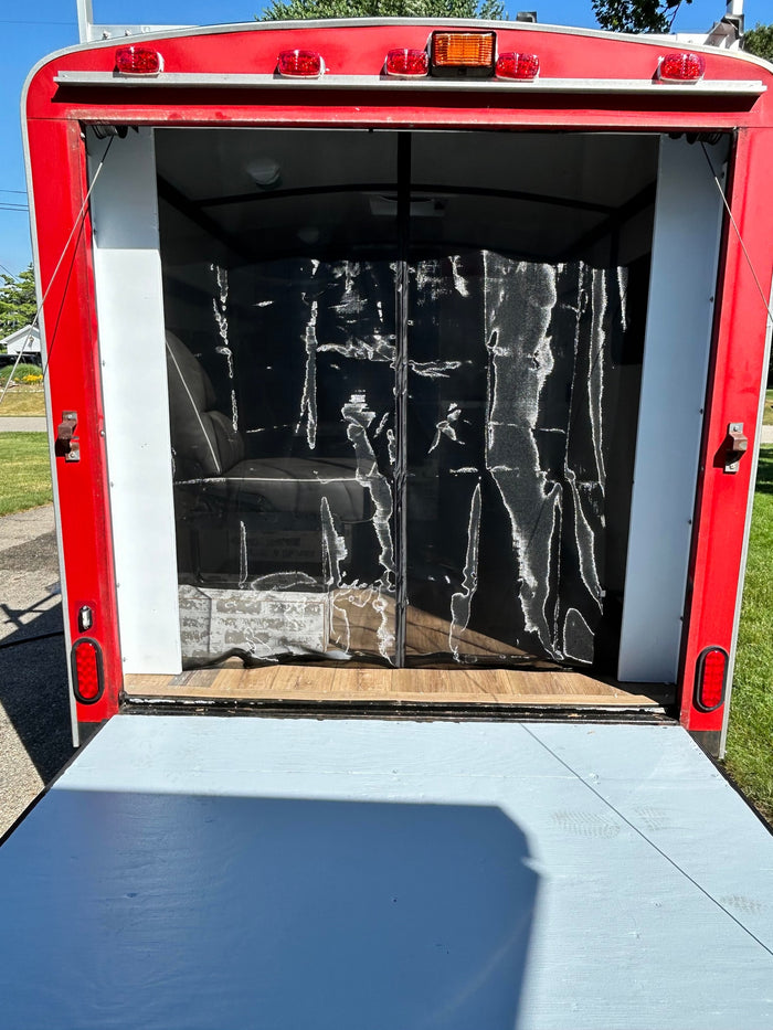 A red enclosed cargo trailer with its rear ramp lowered, revealing the interior with a black privacy curtain. Suitable for RV rental needs.