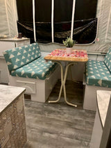 This RV rental features a compact, updated dinette with stylish cushions & a plant, perfect for meals on the road.