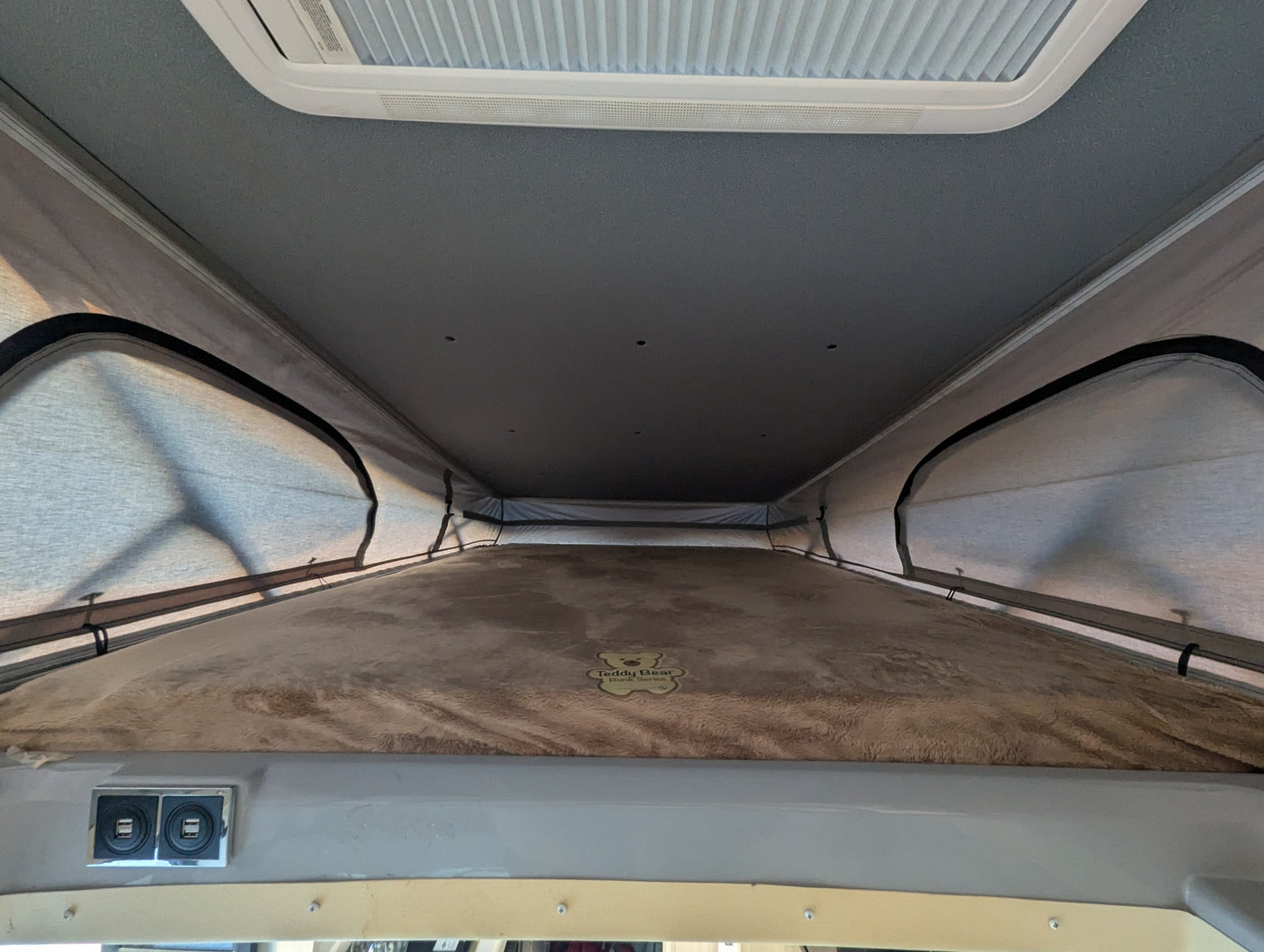 Interior of an **rv rental** pop-top, showing a plush sleeping bunk, USB charging ports, and overhead vent.