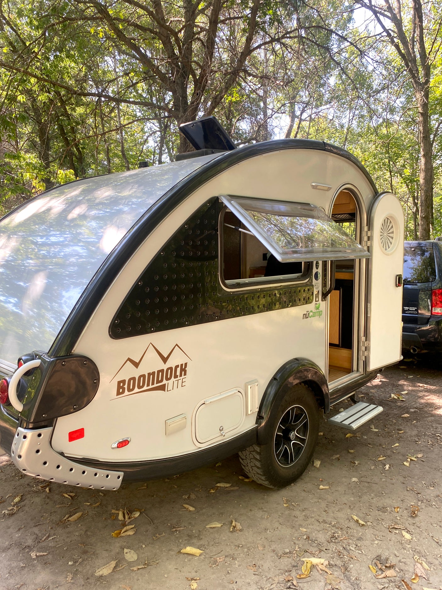 This Boondock Lite teardrop camper RV rental is parked at a wooded campsite, ideal for outdoor adventures.