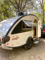 This Boondock Lite teardrop camper RV rental is parked at a wooded campsite, ideal for outdoor adventures.