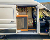 Inside this white RV rental van, a custom conversion reveals a compact kitchen with a sink, plus a colorful bench and front cab.