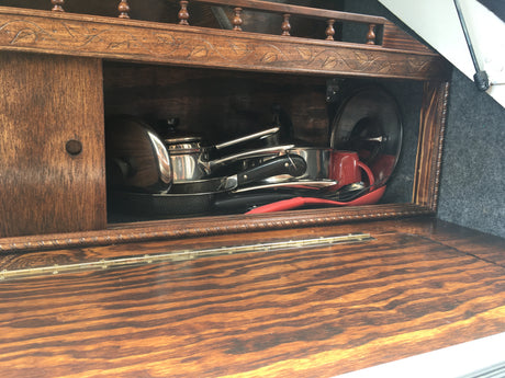 RV rental kitchen: a compact wooden cabinet showcasing neatly stored pots, pans, and utensils, perfect for travel cooking.
