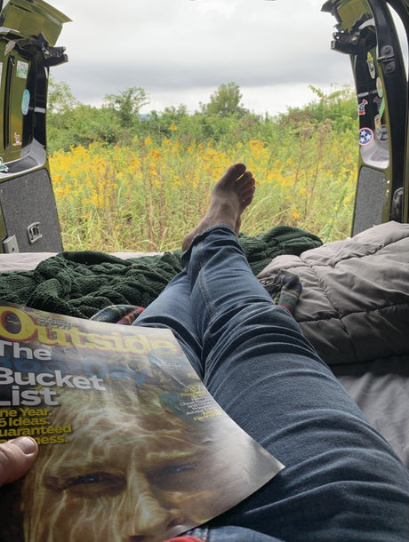 Enjoying an RV rental view of goldenrod fields while reading 'Outside' magazine's bucket list.