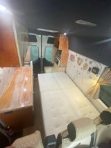 Experience comfort in this stylish RV rental interior, featuring a cozy bed, kitchenette, and custom decor.