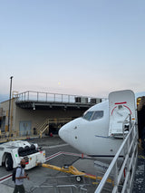 A large white airplane at an airport gate, with people boarding via stairs. A tow tug is nearby. Unlike an **rv rental**, this is air travel. Moon visible overhead.