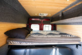 RV rental: Camper van interior with cozy bed, wood/carpet walls, mesh storage, and ceiling fan.