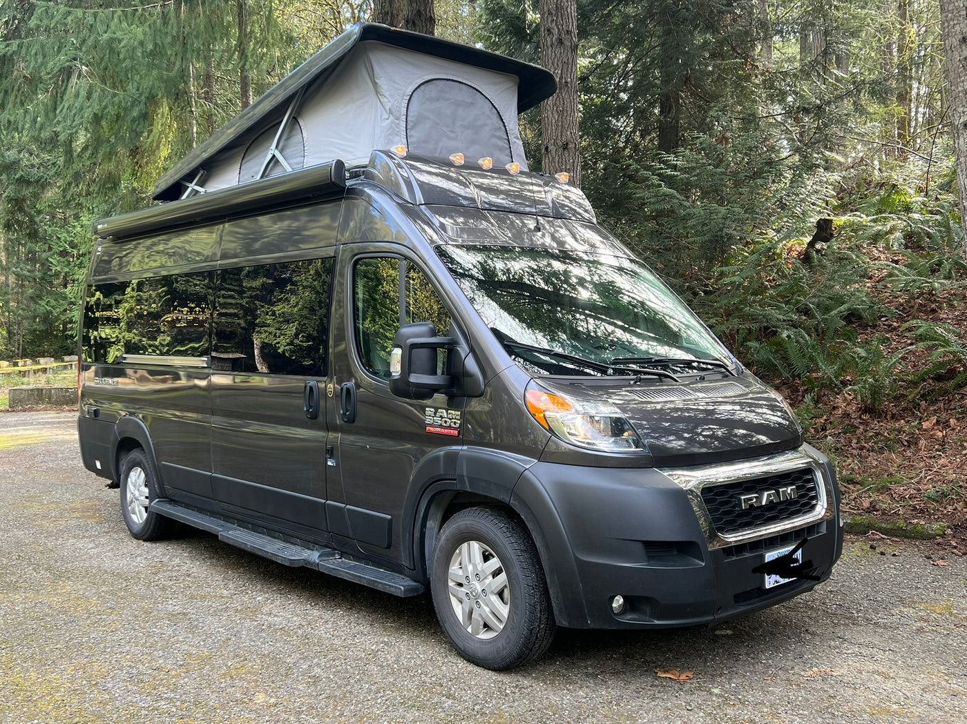 Dark grey Ram ProMaster camper van with pop-top in a wooded setting, perfect for your next RV rental adventure. — photo 14