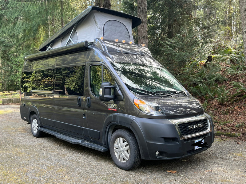 Dark grey Ram ProMaster camper van with pop-top in a wooded setting, perfect for your next RV rental adventure. — photo 14