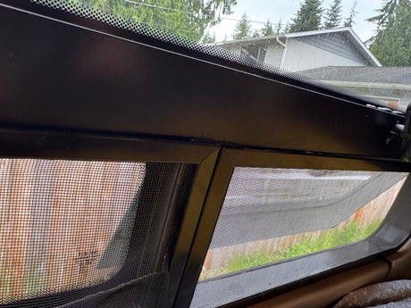 Inside an RV rental, a dark-framed, screened window provides ventilation and a view of the outdoors.