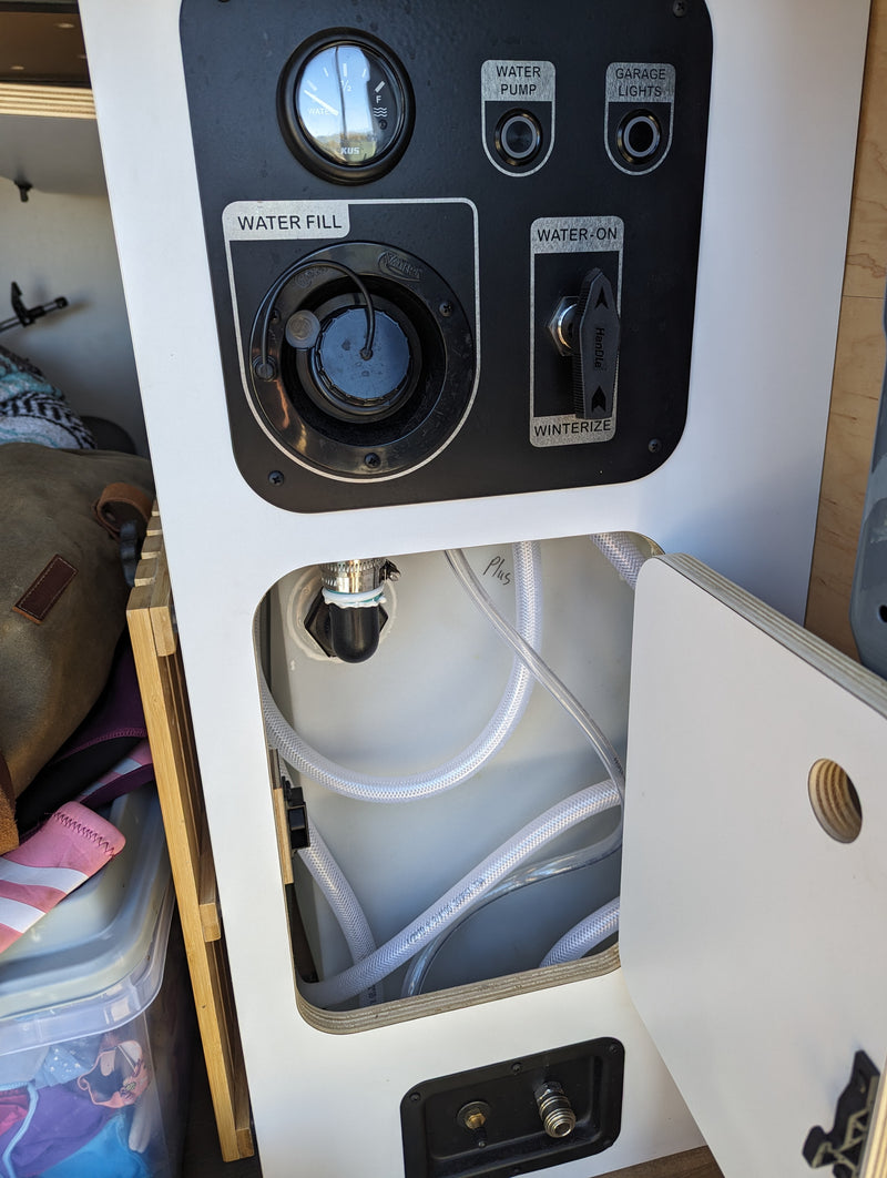 RV rental water system panel: water fill, pump, level gauge, and winterize valve. Hoses connect to the tank below. — photo 13