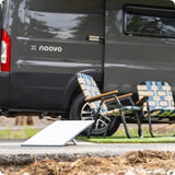 Relaxing with a noovo RV rental: a gray camper van, two striped folding chairs, and a white portable panel outdoors.