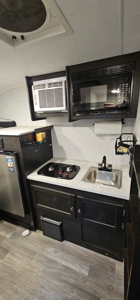 Inside an RV rental: a compact kitchen featuring a stove, sink, microwave, fridge, and wall AC unit.