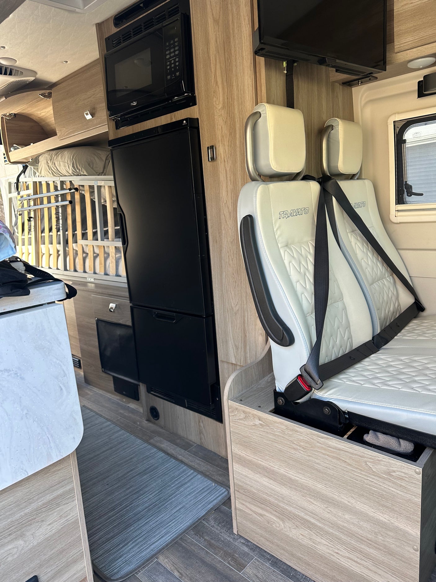 RV rental interior: Winnebago Travato camper van with kitchen, two seats, and baby crib setup for travel.