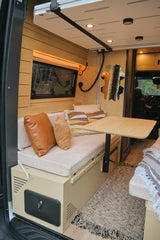 RV rental interior: wood-paneled walls, cushioned bench seating, a functional table, and decor create a cozy, travel-ready space.