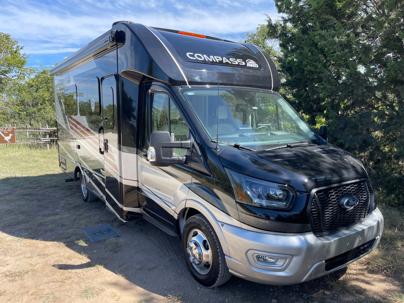 A black and silver Compass AWD motorhome, perfect for an RV rental, is parked at a sunny campsite near a wildlife trail. — photo 7