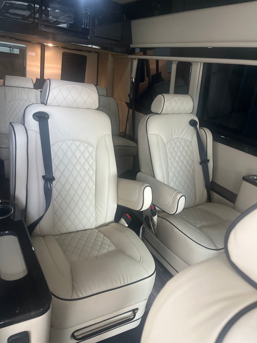 Inside an RV rental, showcasing plush white quilted leather seats with black piping & seatbelts. A spacious, luxury interior.