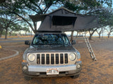 Gray Jeep Patriot with a Nomadic rooftop tent & extended ladder. A unique RV rental for camping adventures.