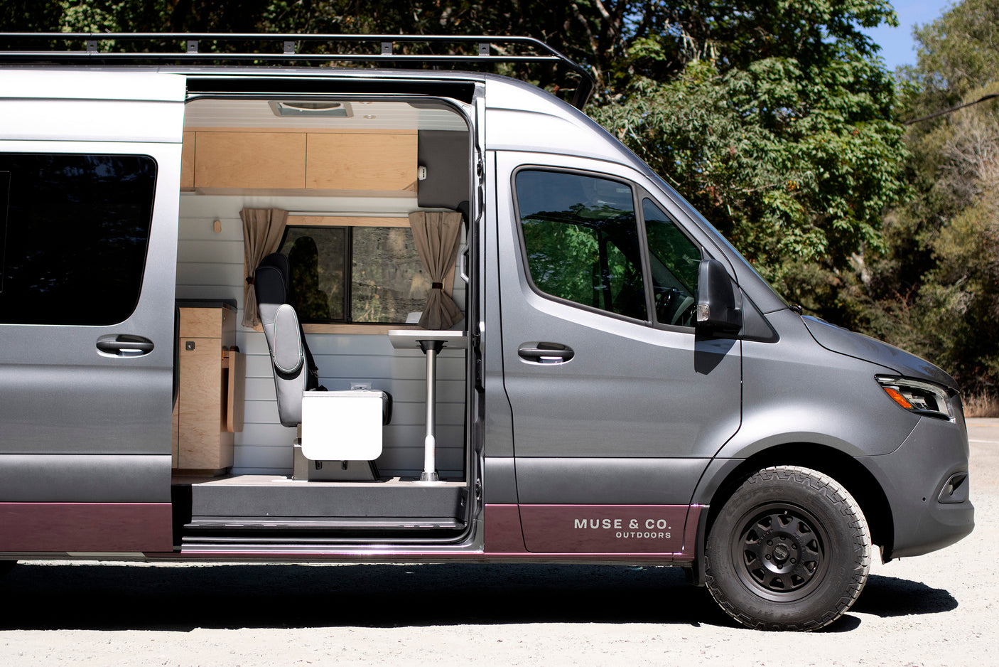 A grey custom camper van with its side door open, revealing a comfortable, woody interior setup, ideal for an RV rental adventure.