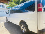 A clean white passenger van with tinted windows, parked on pavement. A versatile vehicle, perfect for an RV rental or travel adventures.
