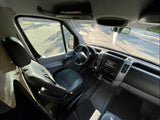 Driver's cabin of an RV rental, showing steering wheel, dashboard, and bright view out the windshield.