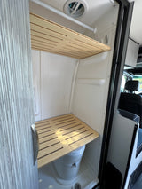 RV rental: Compact camper van wet bath with toilet, shower, and functional slatted wooden shelves, maximizing small space utility.