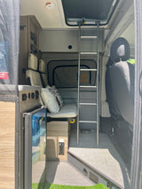 View inside a modern RV rental featuring a bunk bed, bench seating, compact fridge, and control panel for road trip comfort.