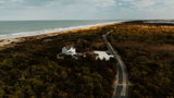 Aerial view of a picturesque coastline, with a winding road leading to a charming house. An RV rental adventure awaits!