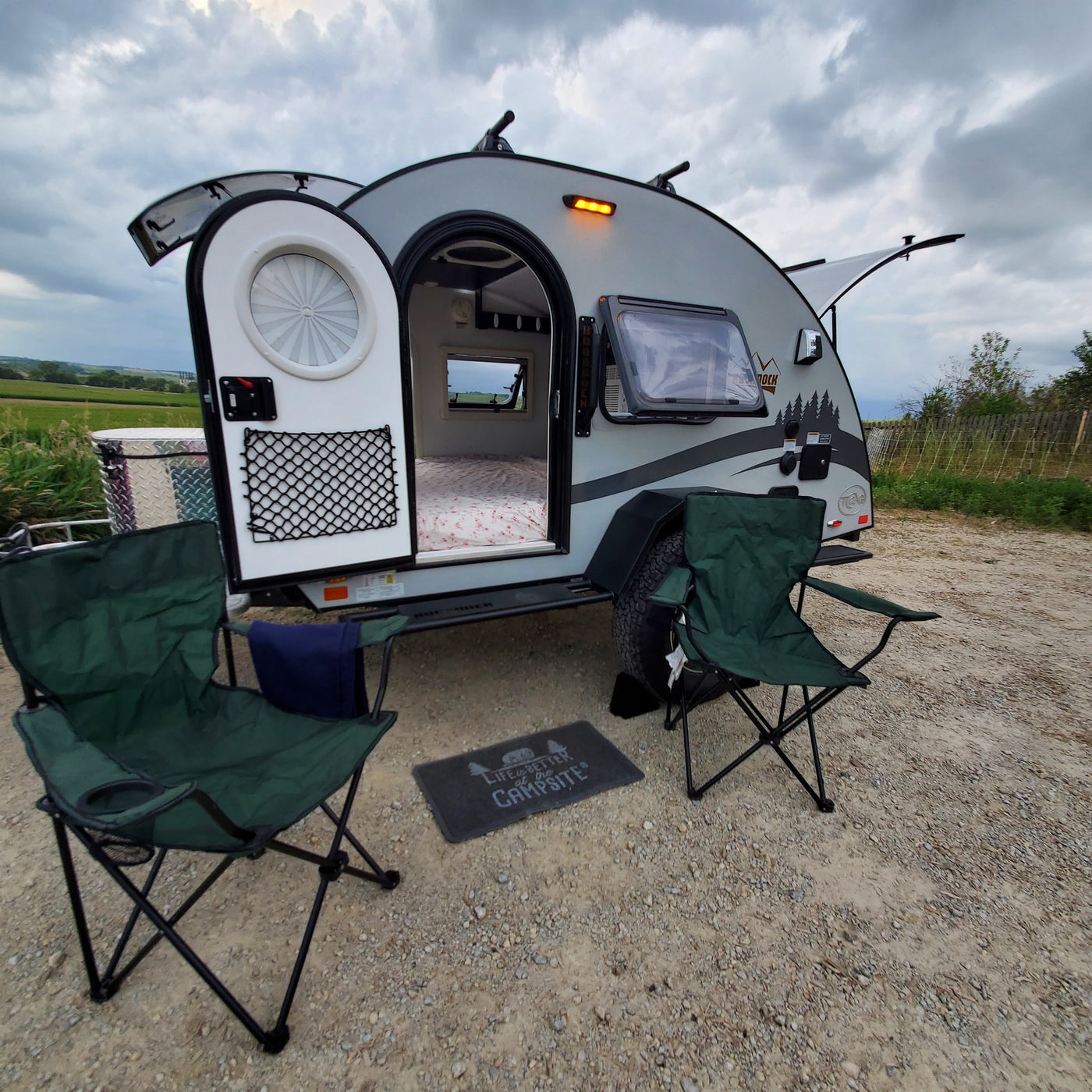 This RV rental teardrop camper is set up for a relaxing stay, with open door revealing the bed, chairs, and a welcome mat outside. — photo 17